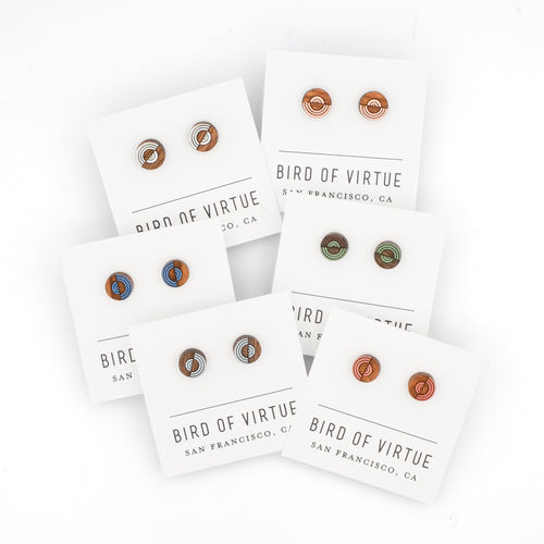 Assortment of colorful circle-shaped wooden stud earrings on white Bird of Virtue cards against a white background. Colors are silver, peach, deep sea, green, powder blue, red clay